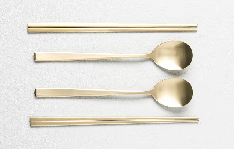A set of gold-colored traditional Korean metal chopsticks and spoons (Sujeo) arranged neatly on a white background.